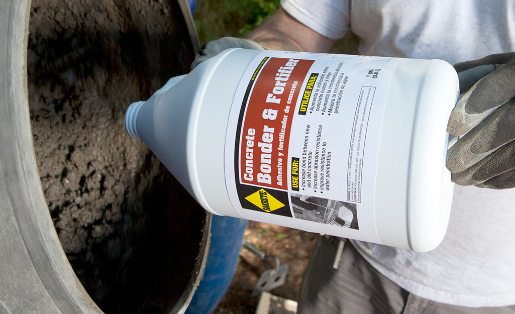 Someone pouring concrete bonder and fortifier from a bottle into cement mix.