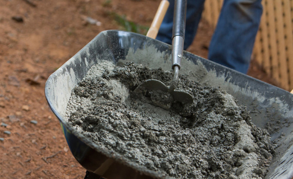 Someone using a hoe to mix concrete in a wheelbarrow.