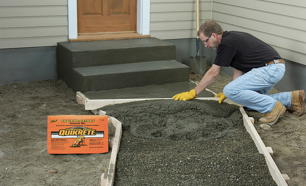 Someone using concrete and a mold to build steps and a walkway from a house.