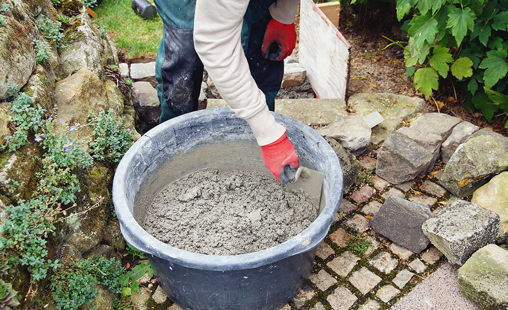Someone wearing gloves to protect their hands while mixing cement in a container.