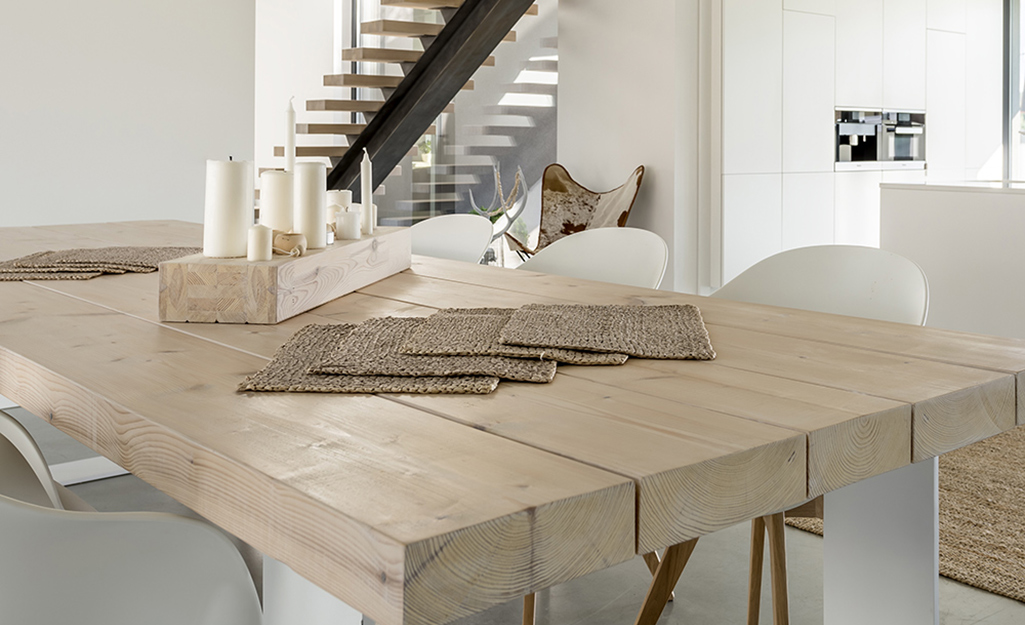 A natural wood table with painted white legs stands in a dining room.