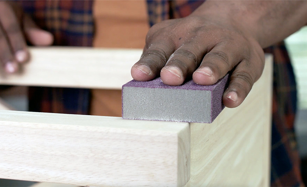 A person sands wood with a sanding block.