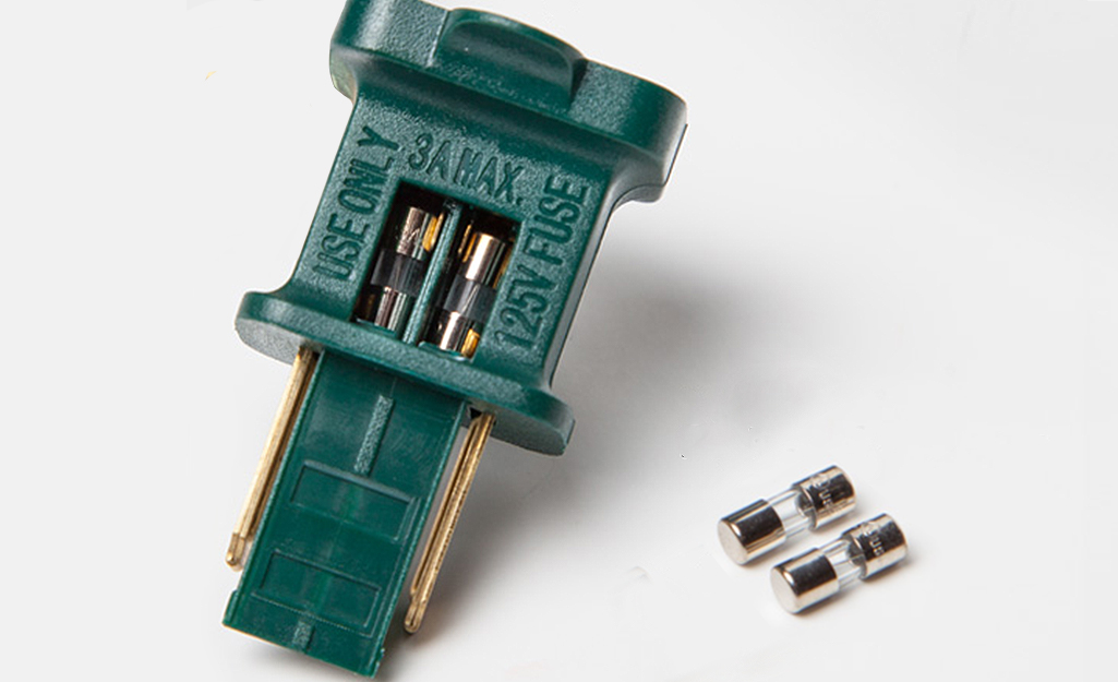 A plug fuse compartment is opened to reveal two glass fuses, while two replacement fuses sit nearby.