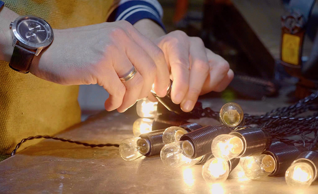 Two hands screw a replacement light bulb into a socket on a strand of string lights.