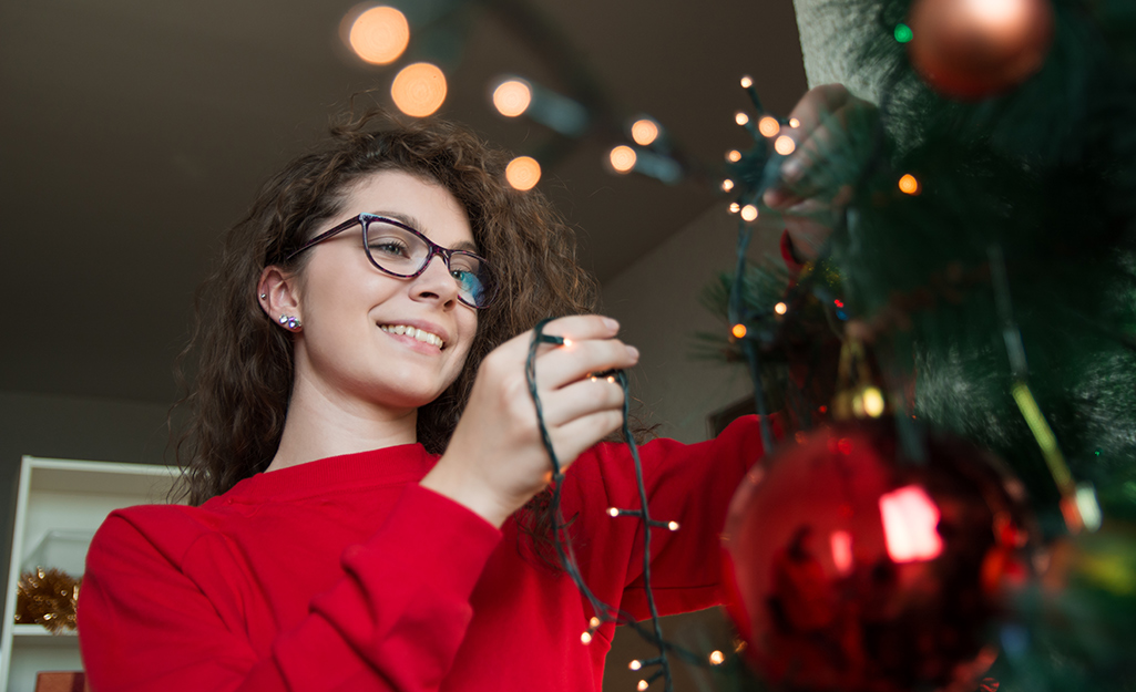 A woman carefully removes a strand of Christmas lights from a decorated tree.