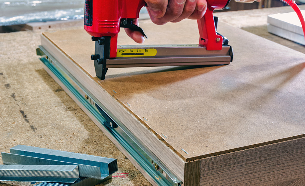 A drawer bottom panel being stapled in place with a staple gun. 