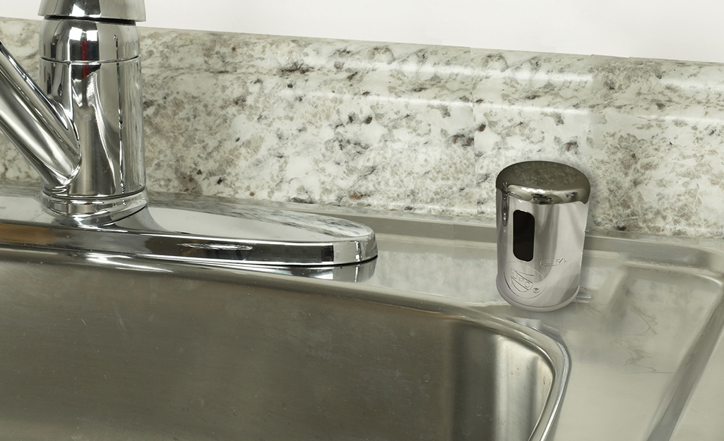 The air gap cylinder is next to the faucet of a stainless steel sink.