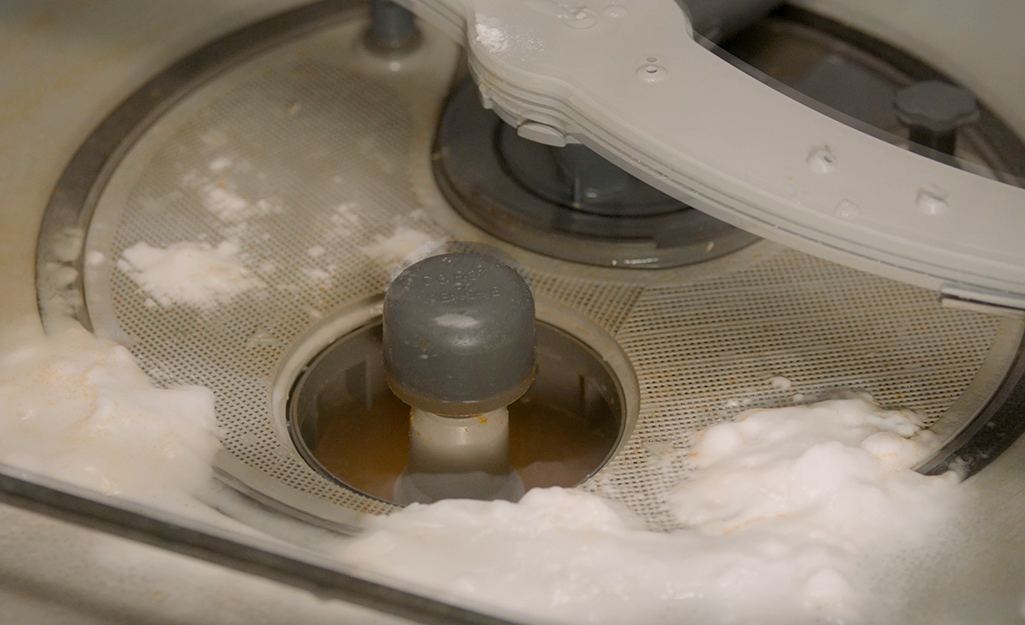 A solution of baking soda and vinegar stands in the bottom of a dishwasher that’s not draining.