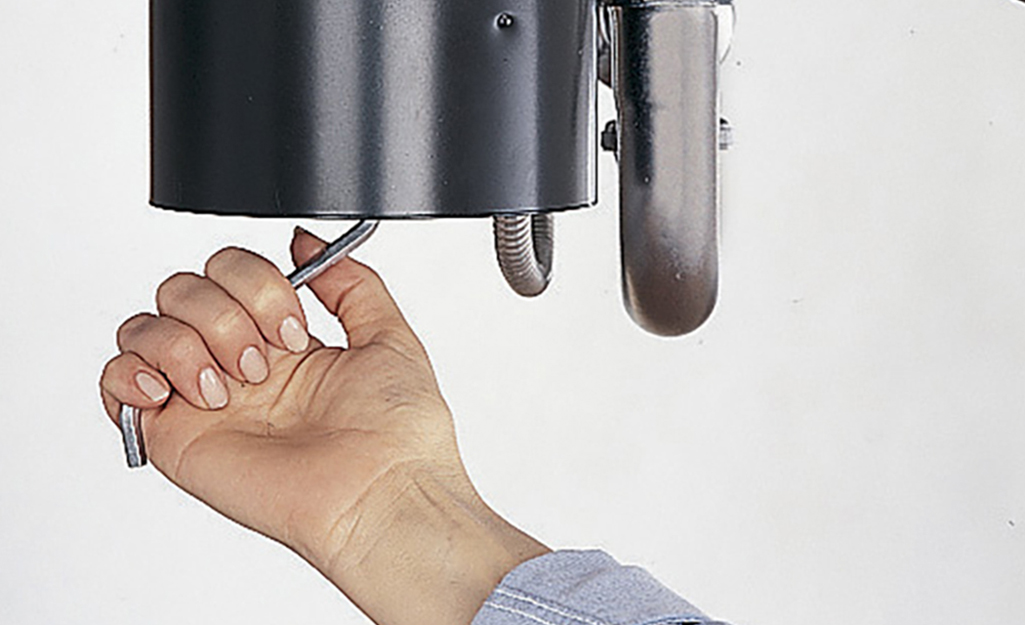 A person reaches under a garbage disposal with a tool to rotate the impeller plate.