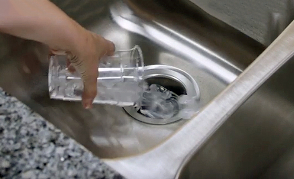 A cup of ice is poured into a garbage disposal.
