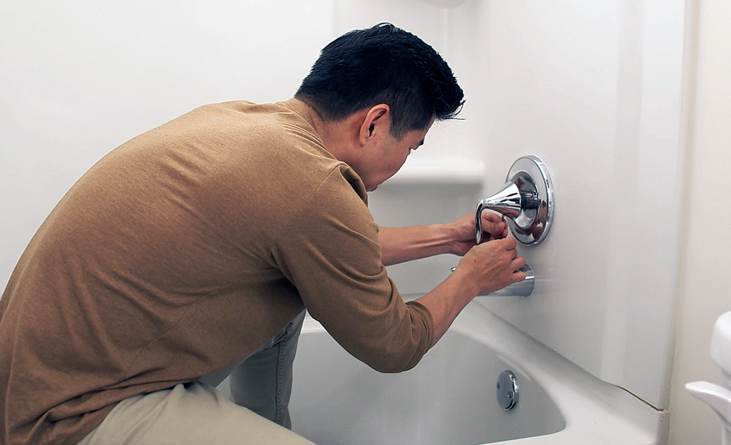 A person reattaching a bathtub faucet handle.