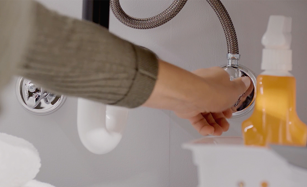 A person reaches under the sink to shut off the water supply.