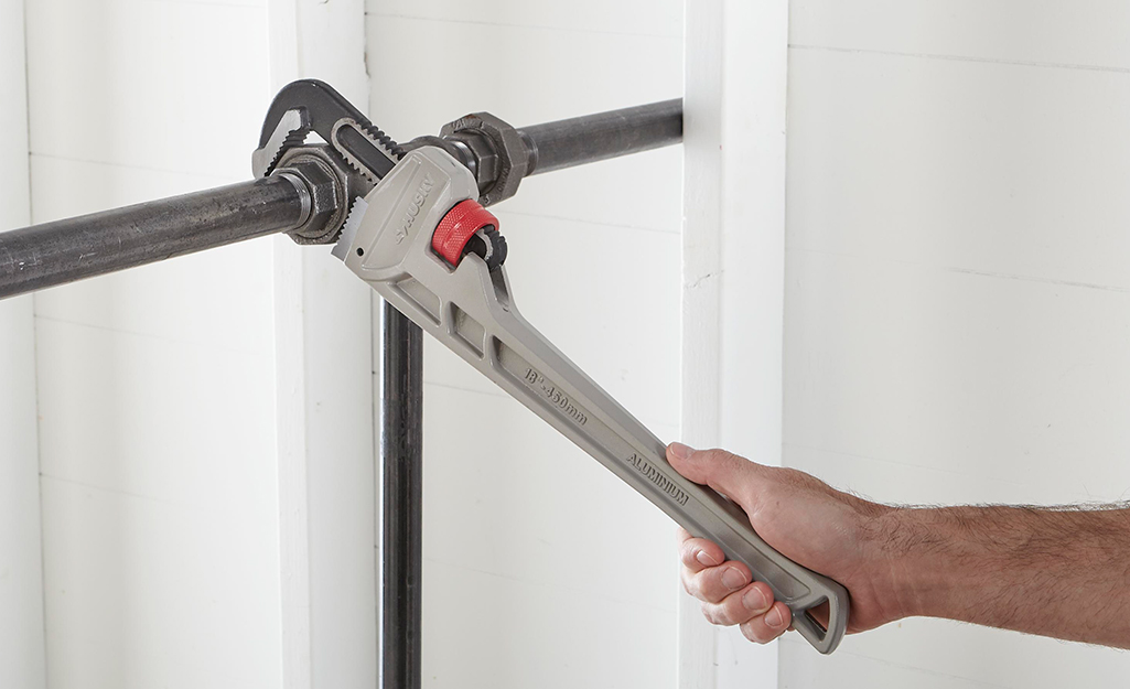 A person uses a wrench to work on plumbing pipes. 