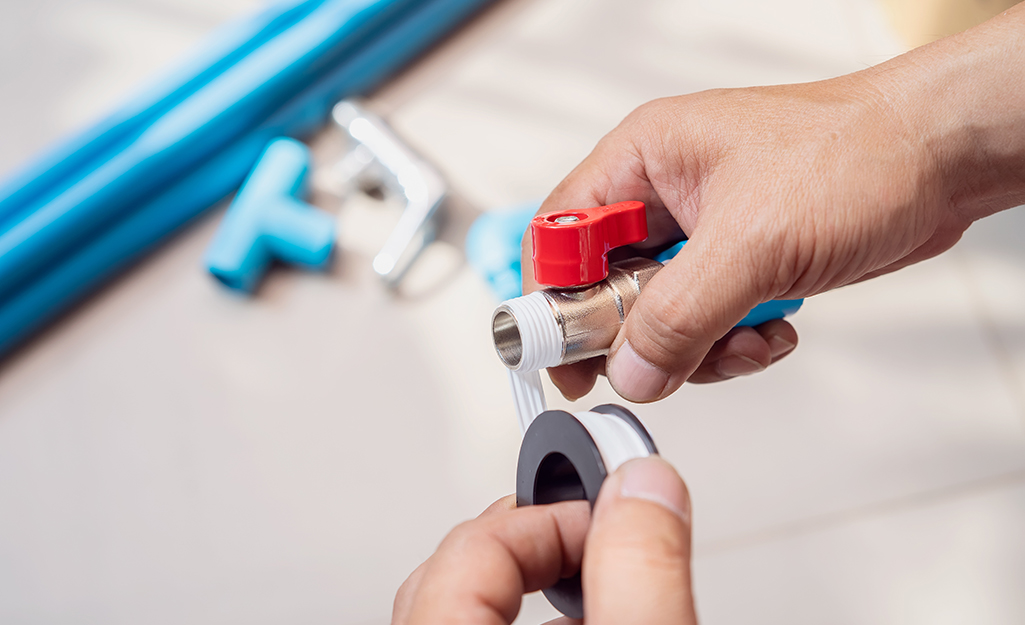 A person applies plumbers tape to the thread of a pipe joint.