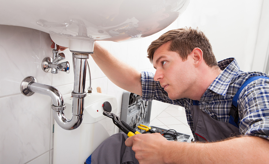 A person looks over a bathroom sink pipe after making repairs. 