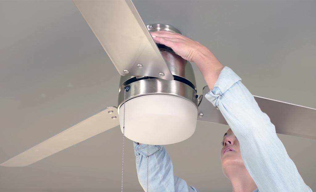A woman adjusting the canopy of a ceiling fan