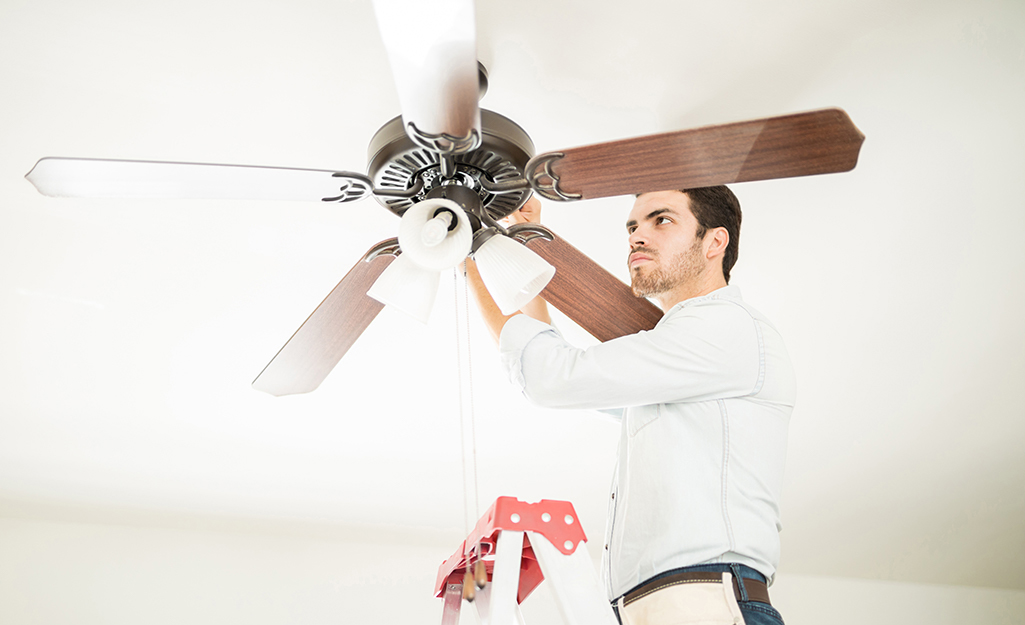 A man adjusting a ceiling fan while standing on a ladder