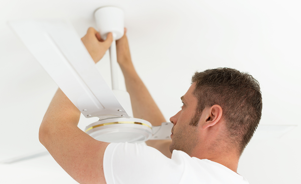 A man adjusting the canopy of a ceiling fan A man adjusting the canopy of a ceiling fan