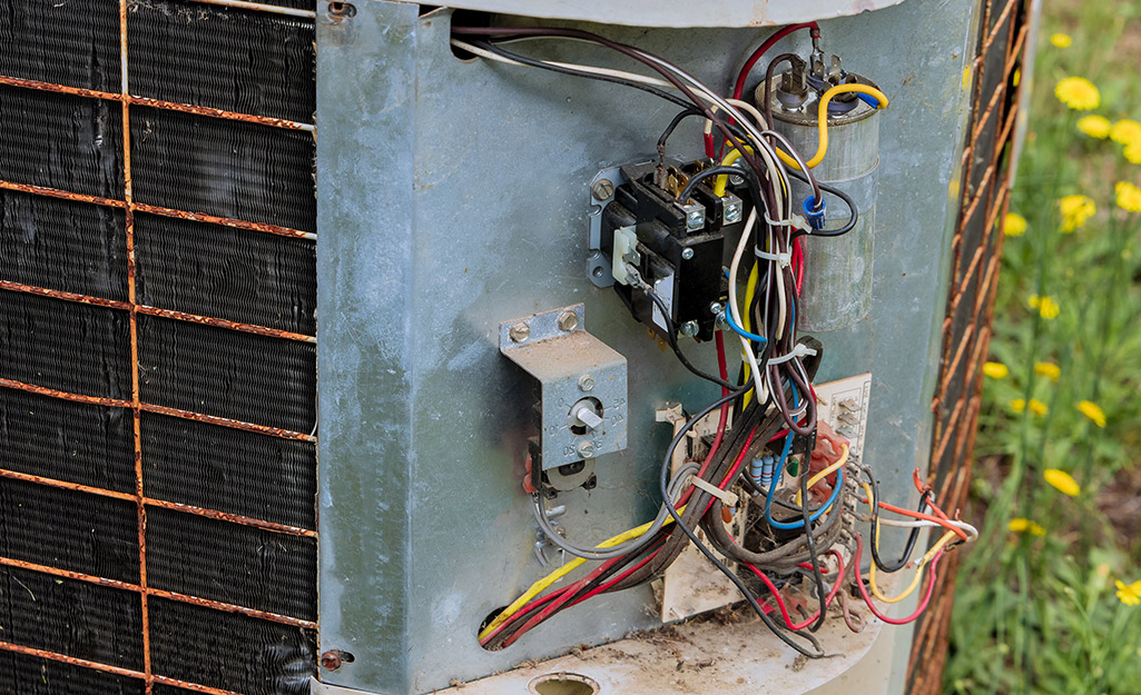 An air conditioner unit with the service panel removed, revealing the capacitor and other components.