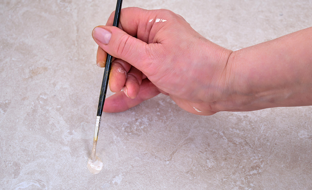 A person uses a paintbrush to apply paint to fix a small crack in a floor.