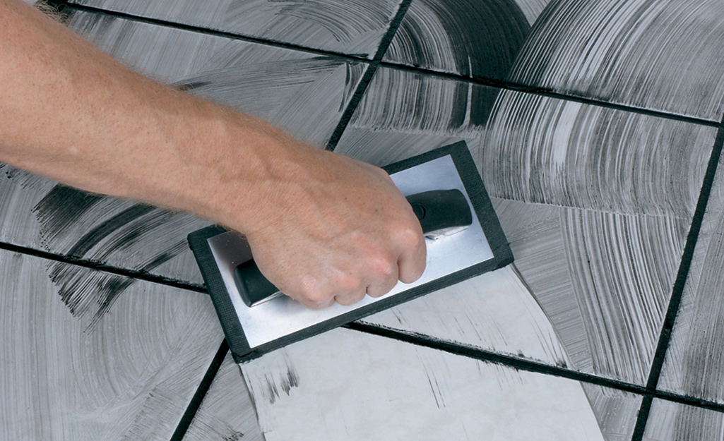 Using a diagonal motion, a person applies grout to the tiles of a floor. Using a diagonal motion, a person applies grout to the tiles of a floor.