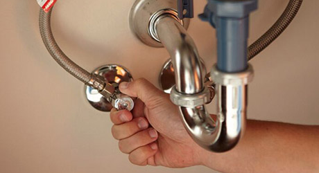 Une personne tourne une vanne d'alimentation en eau sous un évier.