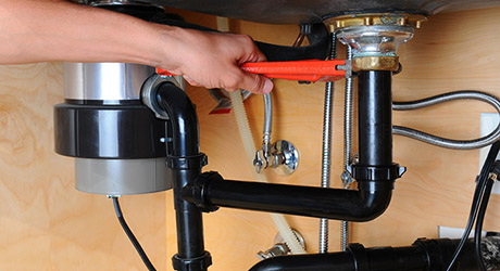 Une personne utilise une clé pour travailler sur les tuyaux de plomberie sous un évier.