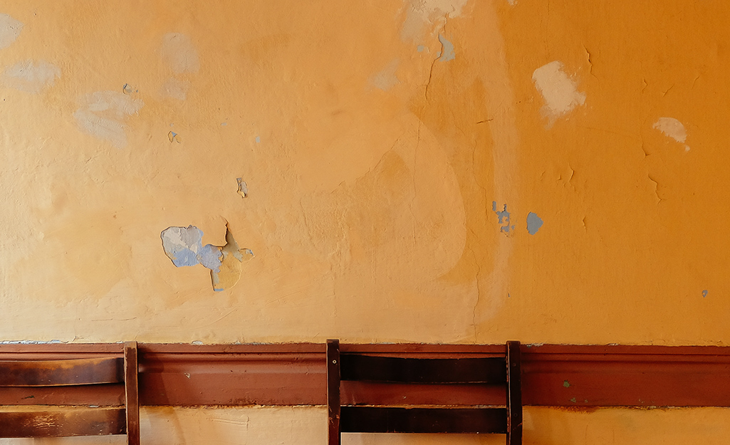 A worn orange wall has areas of chipped and peeling paint.