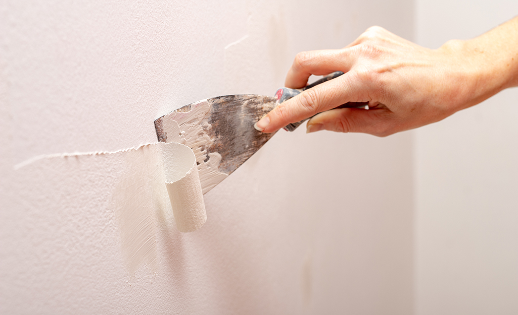 A person scrapes off peeling paint with a putty knife.