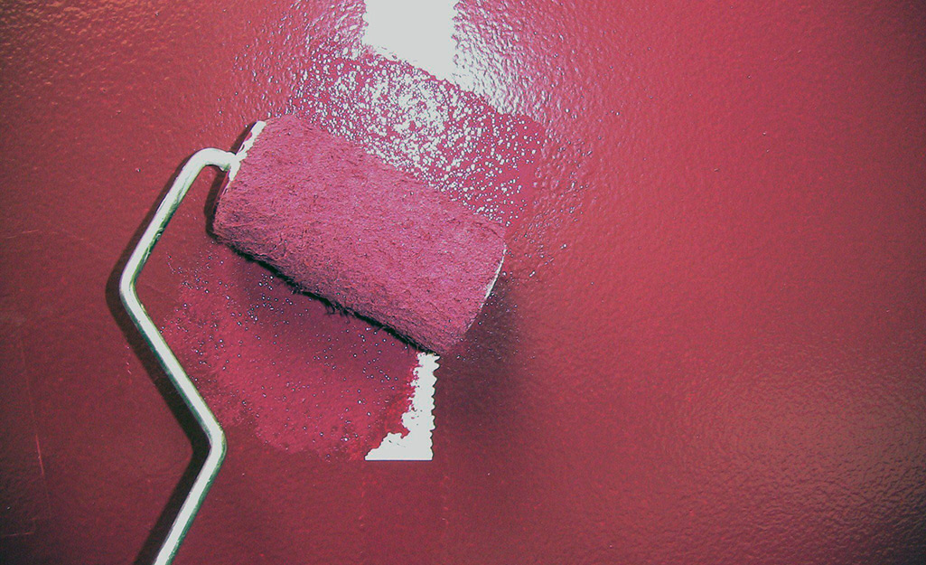 A short paint roller covers a patch with fresh paint to match the wall.
