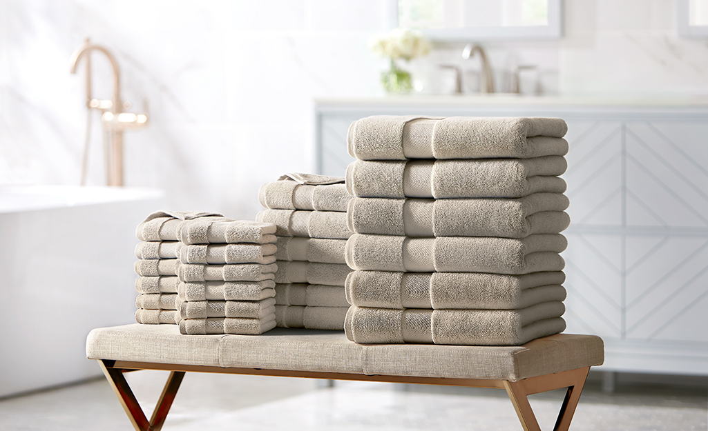 Stacks of folded beige bath towels and hand towels lay on a bathroom bench.