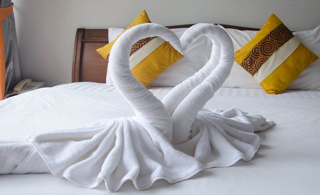 White towels folded into a swan shape on a bed.