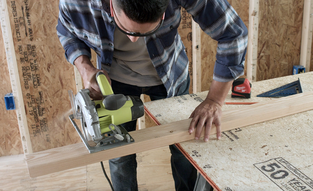 A person using a circular saw to cut king studs for a door frame.
