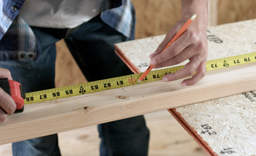 A person measuring and marking a piece of wood for a stud.