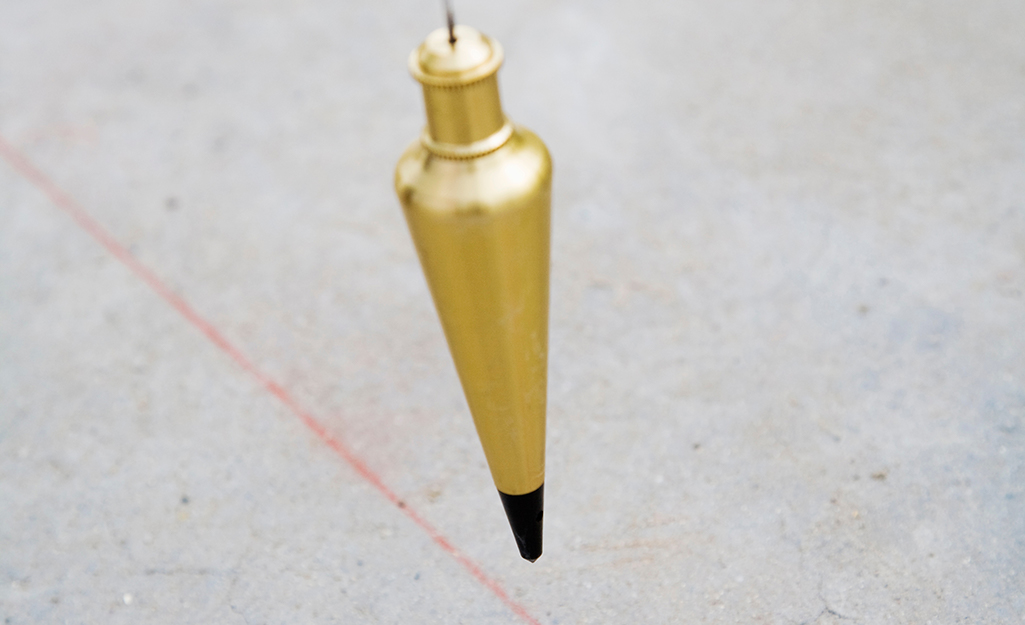 A person using a pencil to mark a spot on the floor underneath a plumb bob. 