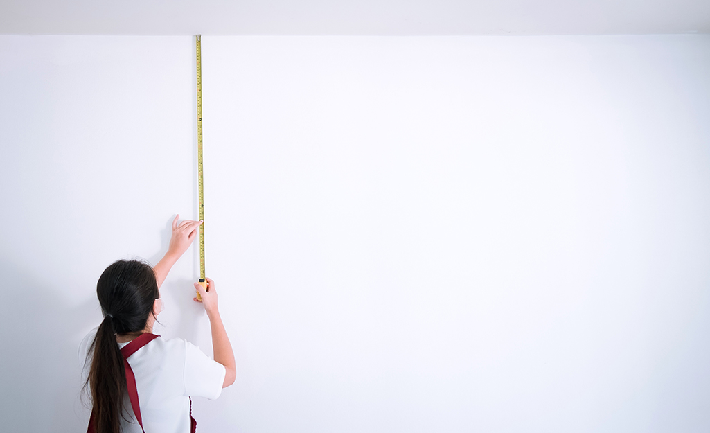 Person measuring stud length between ceiling and floor with tape measure.