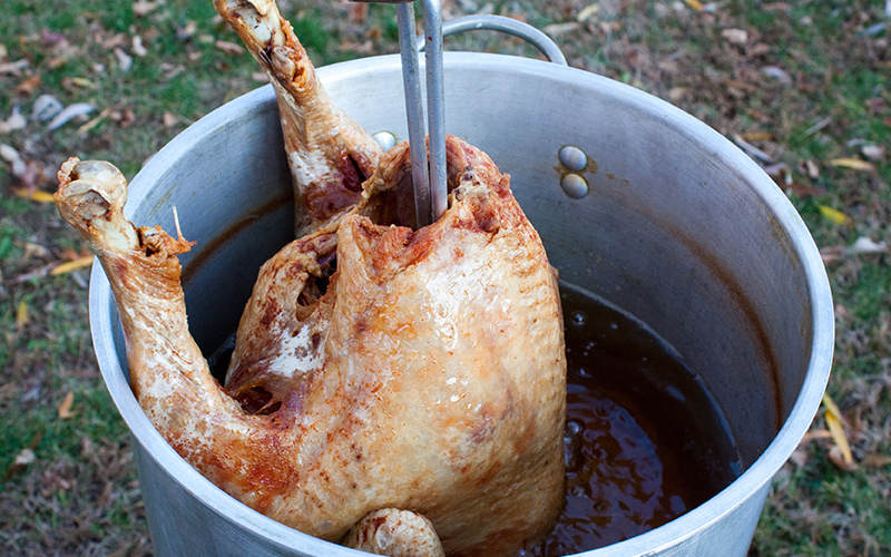 A turkey being lowered into hot oil in an outdoor turkey fryer. A turkey being lowered into hot oil in an outdoor turkey fryer.
