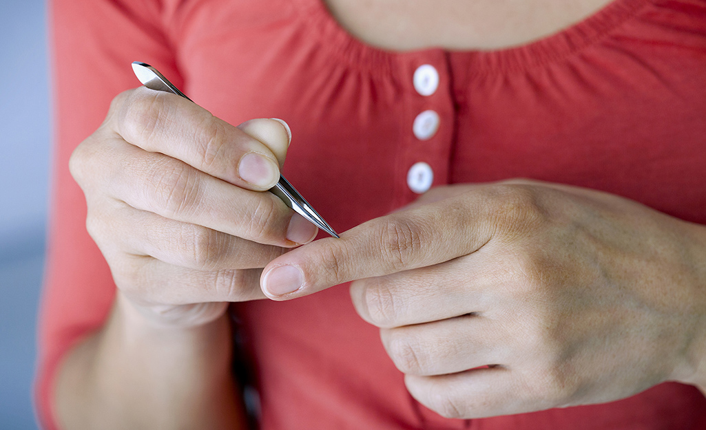 A person uses tweezers to remove a splinter from her index finger.