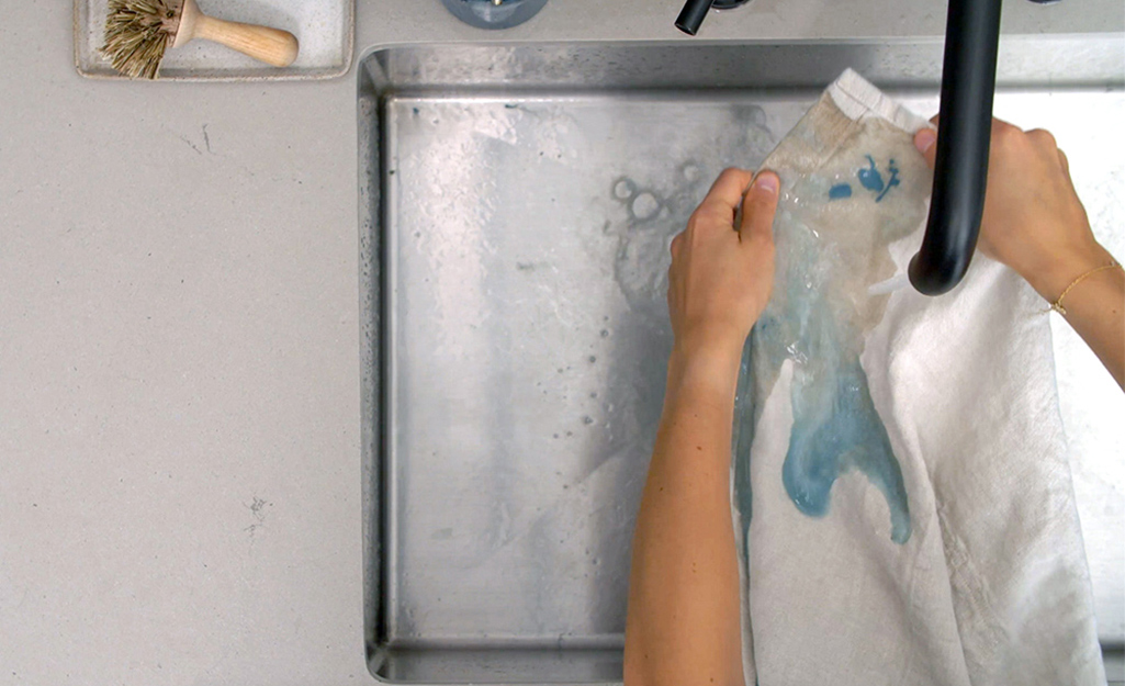 A person uses soap and water to flush an acrylic paint stain from clothing.