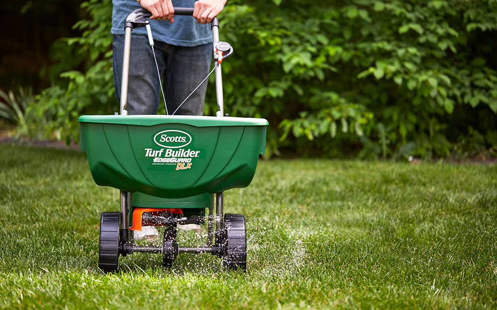 A person pushing a spreader over grass.