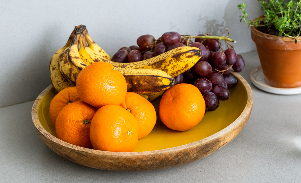 A bowl of fruit including bananas and oranges on a counter.