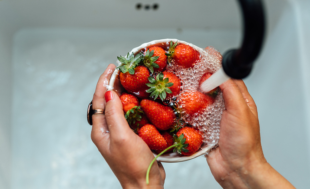 Someone washing fruit over a kitchen sink.