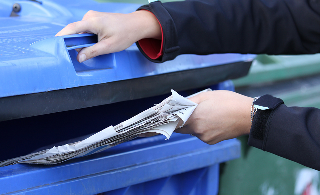 A person recycling old newspapers in a blue bin.