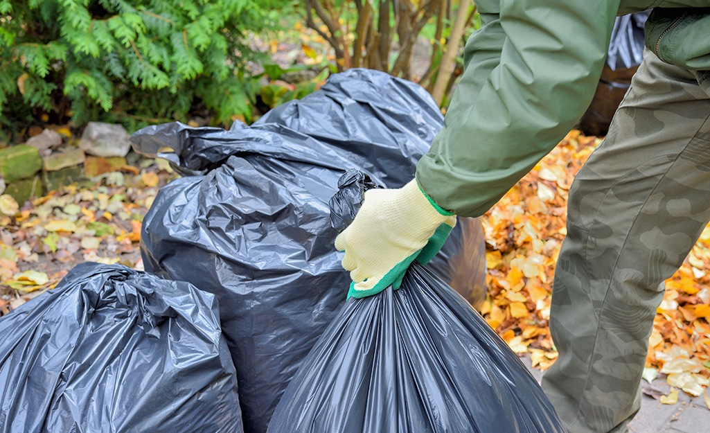 Gardener with gloves removing yard debris in bags