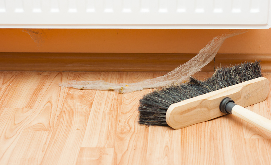 A person uses a push broom to sweep up a cobweb.