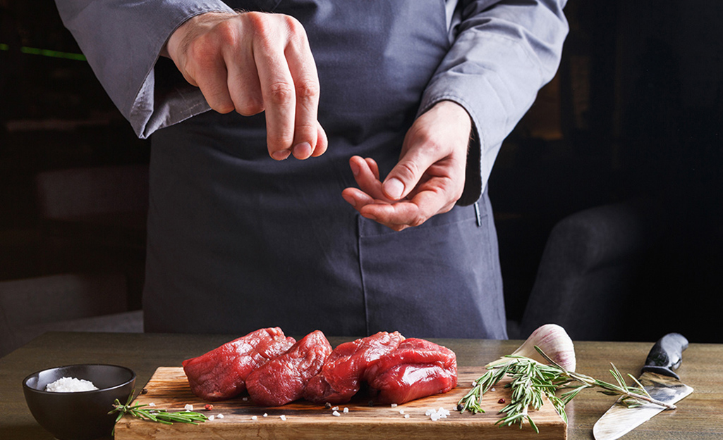 A person seasoning cuts of steak before grilling.