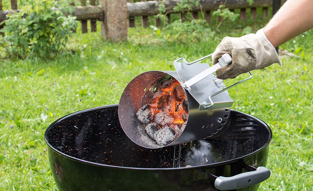 A person pouring hot coals from a chimney into a grill.