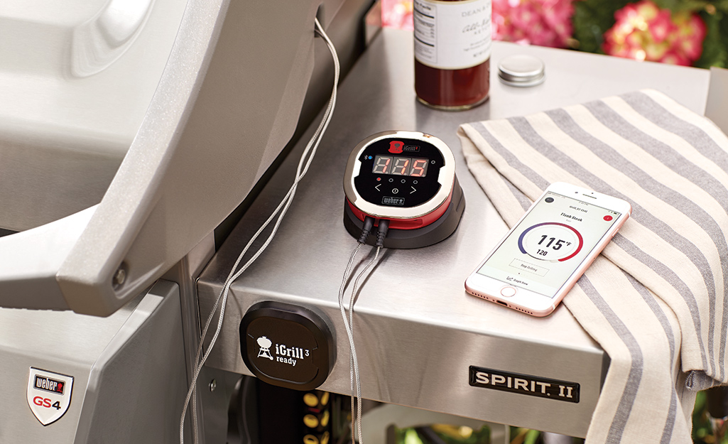 A digital thermometer reading the internal temperature of steaks on a grill.