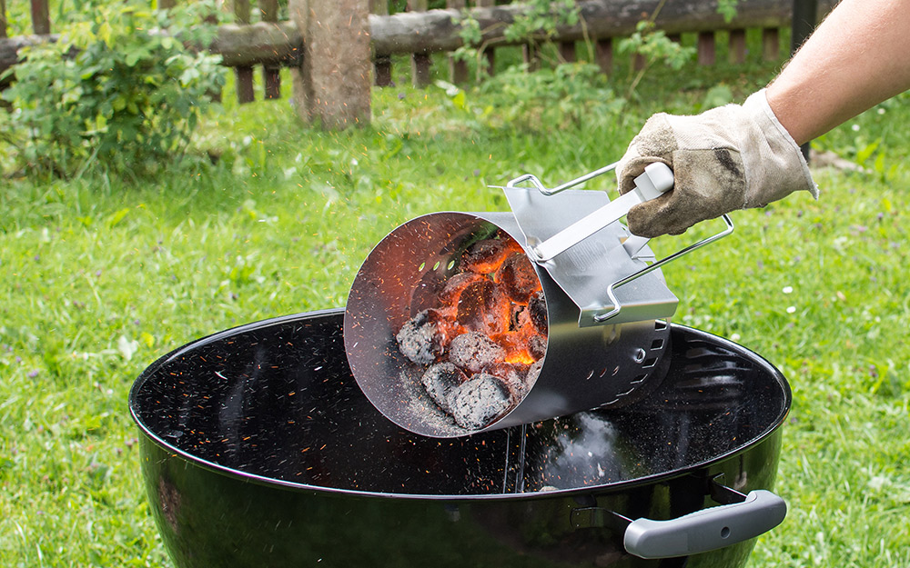 A person pouring hot charcoal into a grill.