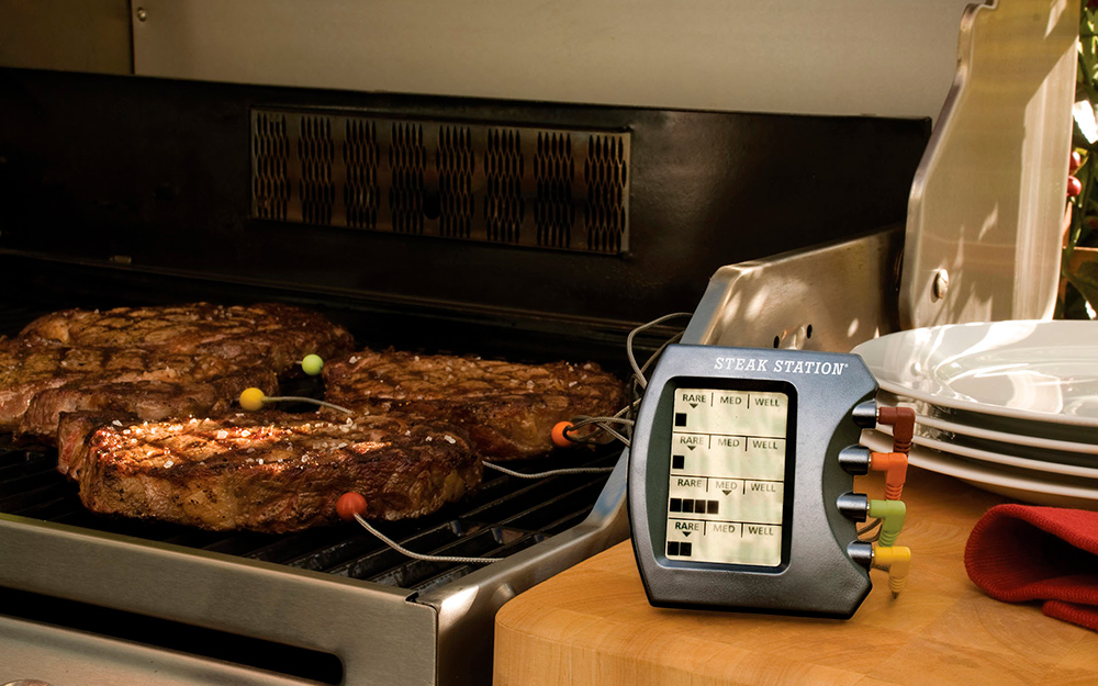 A digital thermometer reading the internal temperature of steaks on a grill.